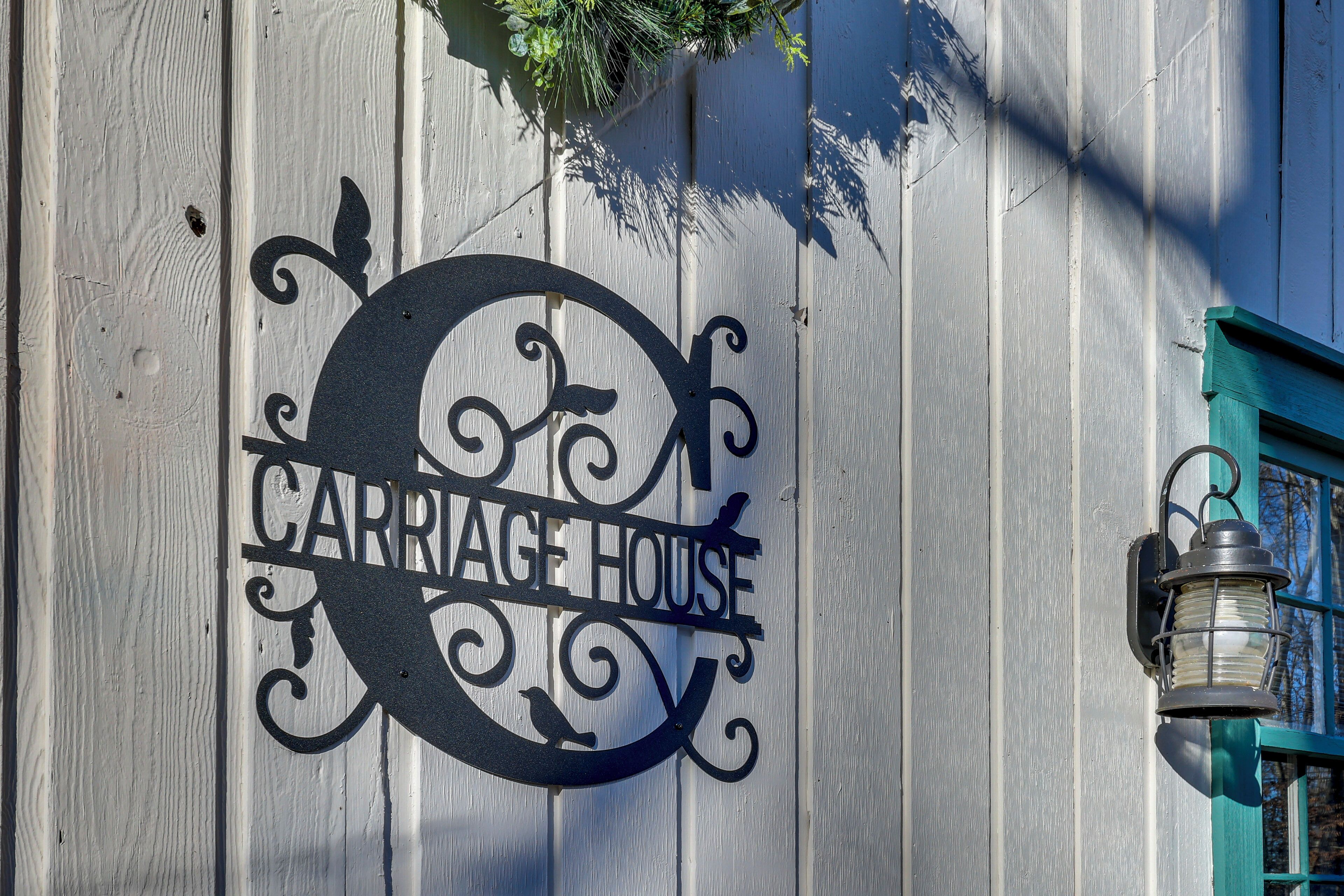 A metal sign with the text "CARRIAGE HOUSE" on a wooden wall.
