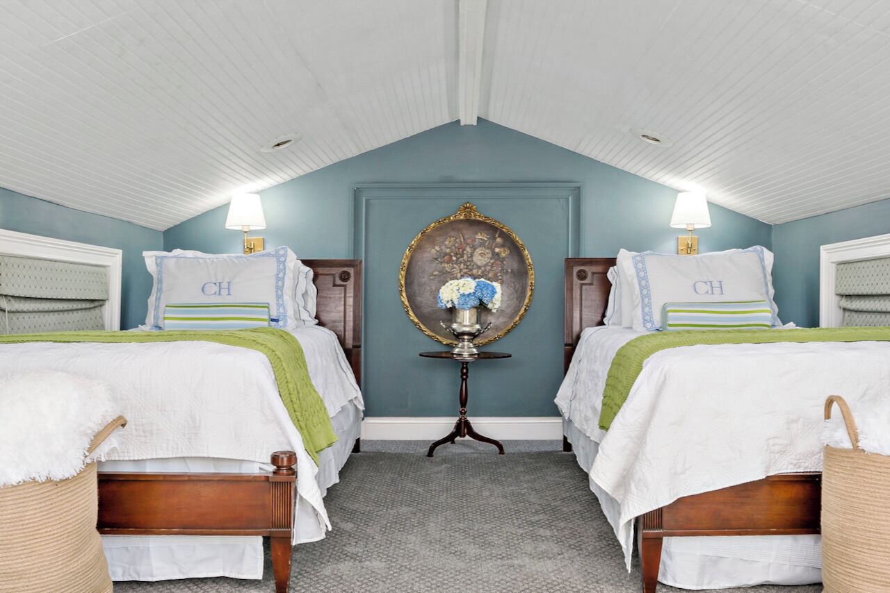 Une chambre avec deux lits, chacun recouvert d’une couvre-lit blanche agrémentée de touches de vert, une petite table avec un miroir et une lampe fixée au mur.