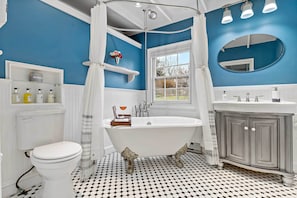 Un baño con una bañera de patas de león, un inodoro blanco, un tocador con espejo y una ventana con vistas al exterior.