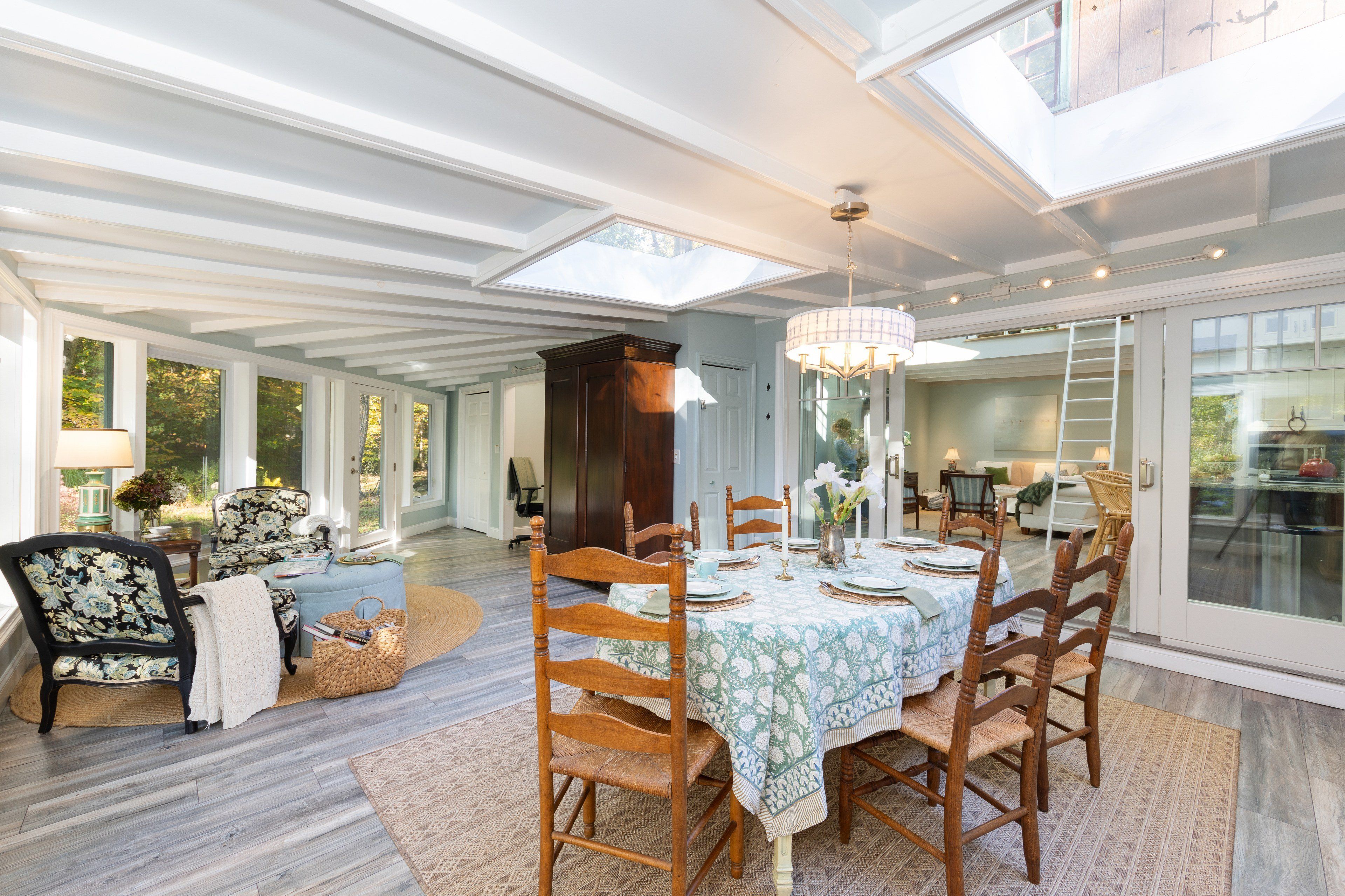 A spacious dining area with a high ceiling and skylights, wooden dining table set for six, and a view of the outdoors through large windows.