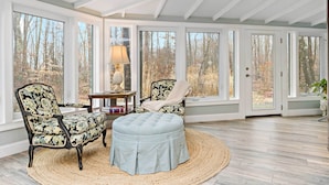 A conservatory with large windows, a wooden floor, and two upholstered chairs with a floral pattern. - Guilford Carriage House at Granite Lodge! (Guilford)