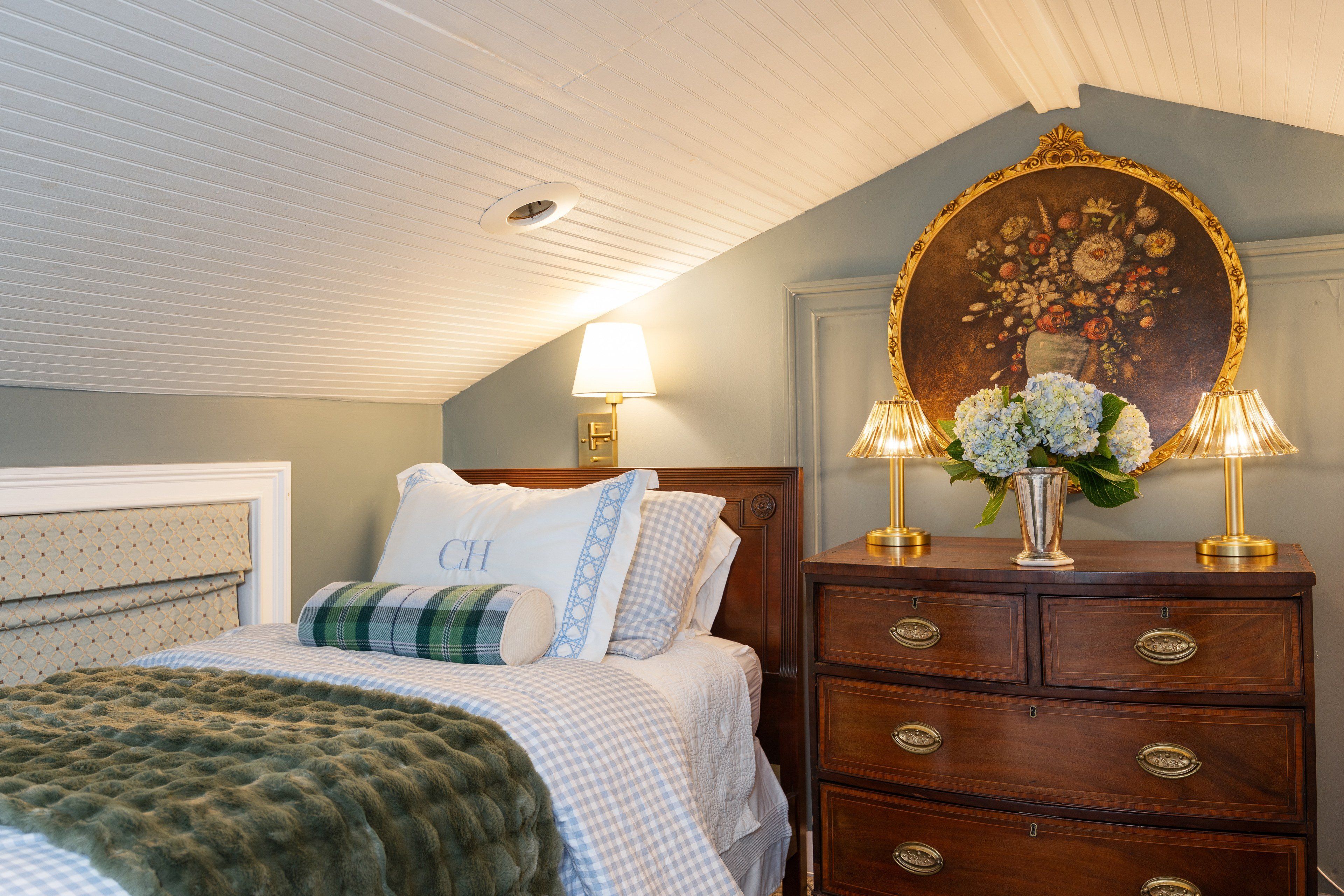 A bedroom with a bed, a dresser with drawers, a mirror with a floral frame, and two lamps.