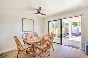 Un comedor con una mesa de madera redonda y seis sillas, un ventilador de techo y un gran ventanal corredizo que da a un patio exterior.