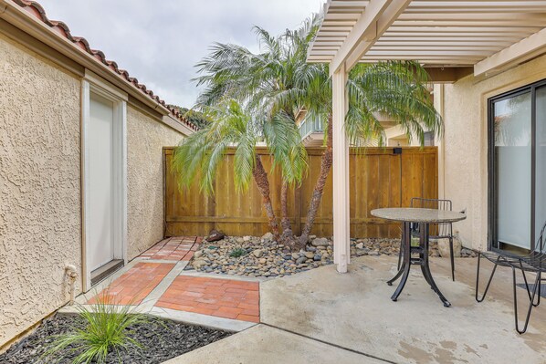 A patio with a table and chairs, a palm tree, and a wooden fence.