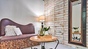 A cozy seating area with a brown sofa, a round wooden table with a lamp, and a rustic wall with a mirror. - Laredo Vacation Rental Near Tourist Attractions! (Laredo)