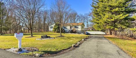 A residential driveway leading to a house with a mailbox, surrounded by trees and a grassy lawn.