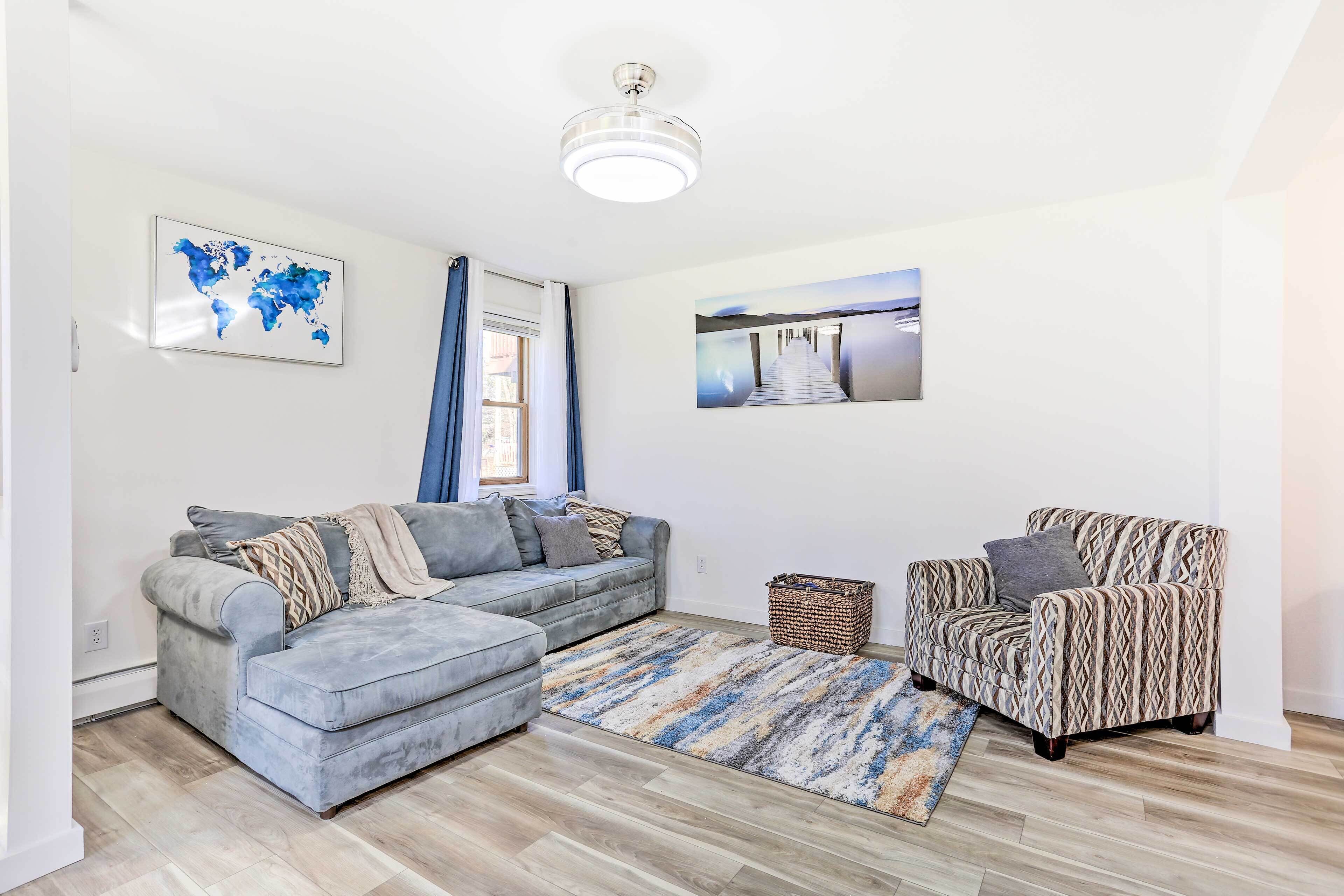 A living room with a grey sofa, patterned armchair, and a blue and beige rug.