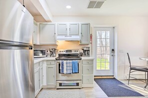 Una cocina con un refrigerador de acero inoxidable, un horno y armarios blancos. Hay una ventana con vista a un paisaje verde.