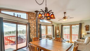 A spacious dining area with a wooden table and chairs, a ceiling fan, and large windows offering views of a deck and trees.