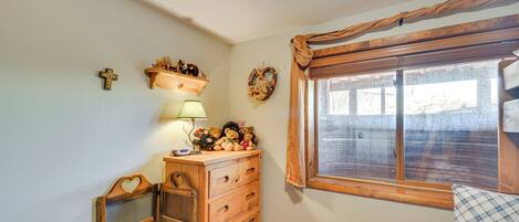 A room with a wooden dresser, a window with curtains, a teddy bear, and wall decorations.