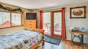 A cozy room with a bed, a television, a desk with a sewing machine, and a sliding glass door leading to an outdoor area.