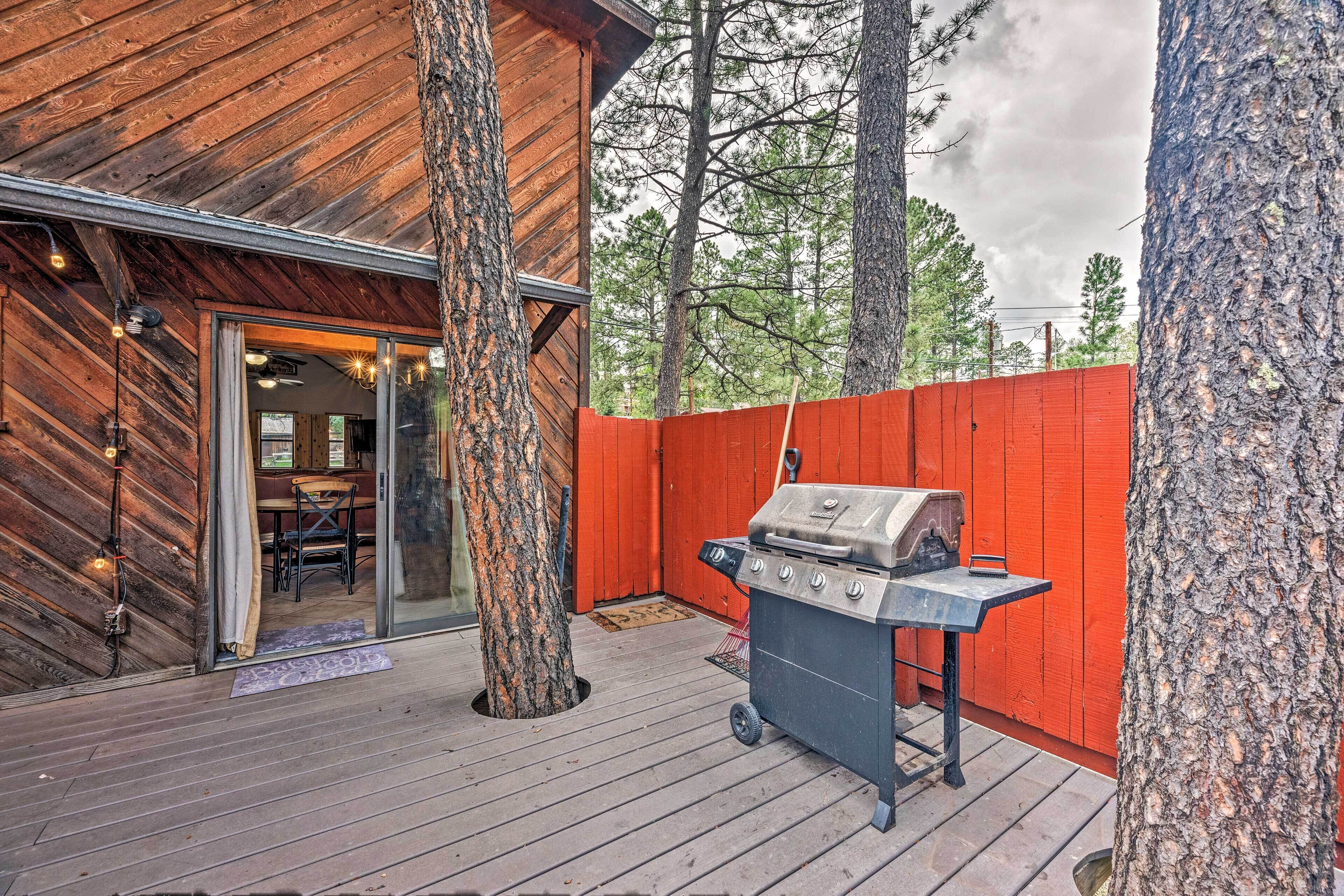 An outdoor patio with a grill, wooden deck, and a red fence.