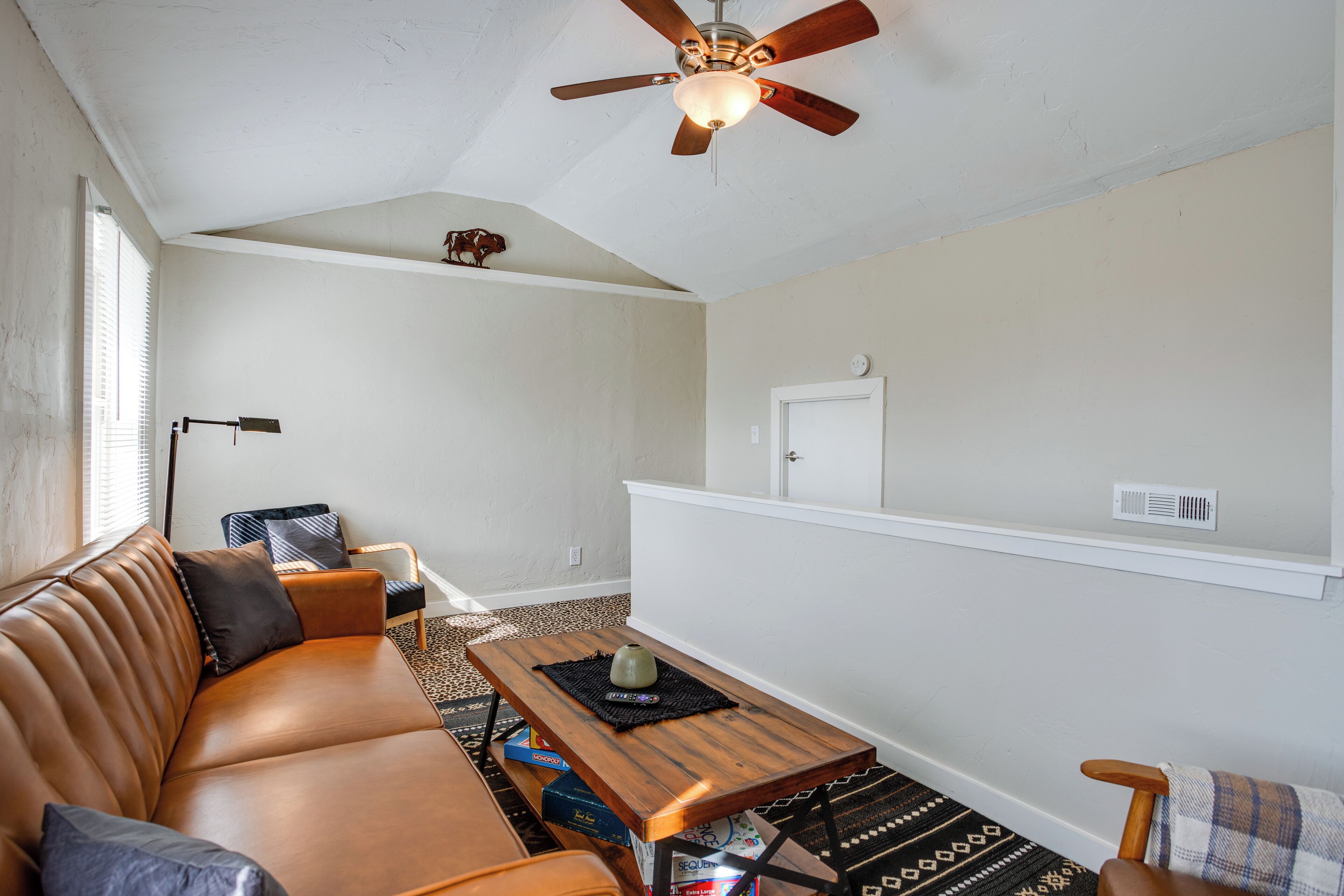 Un salon avec un canapé en cuir marron, une table basse en bois, un ventilateur de plafond et un tapis à motifs.