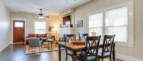 Comedor con mesa y sillas de madera, ventilador de techo y ventana grande con persianas.
