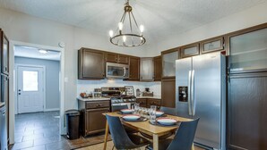 A modern kitchen with stainless steel appliances, wooden cabinets, and a dining area with a table set for four. - Chic Lawton Home, 5 Mins to Fort Sill! (Lawton)