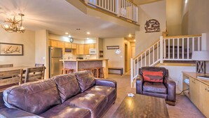 A spacious living area with a leather sofa, a coffee table, and a leather chair. A kitchen is visible in the background with wooden cabinets and a refrigerator. - Walk to Lifts: 'chimney Ridge' Townhome w/ Hot Tub (Breckenridge)