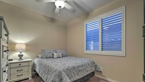 Ein Schlafzimmer mit Bett, Nachttisch, Lampe, Kommode und Fenster mit Jalousien.