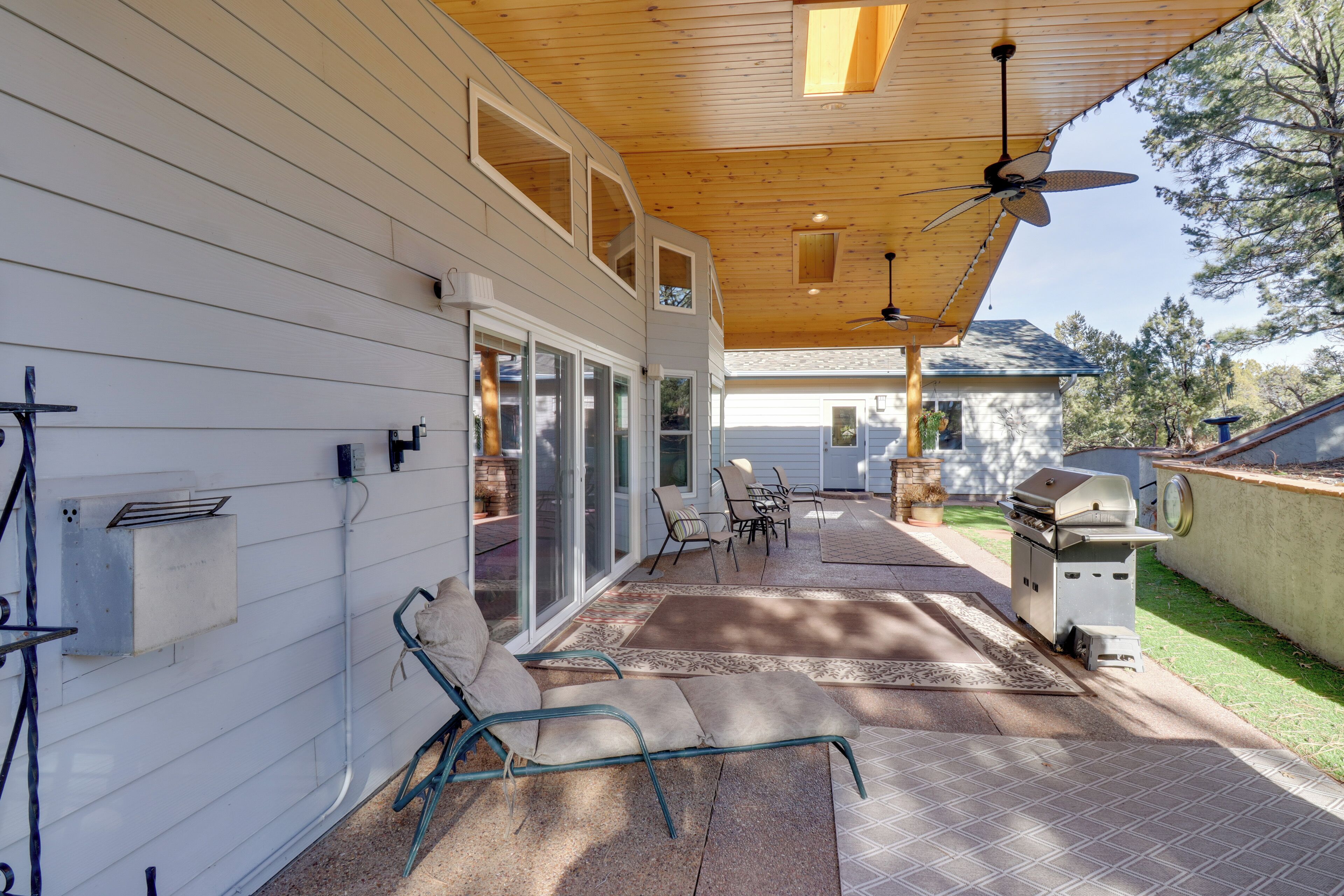 A covered patio with outdoor furniture, a grill, and a ceiling fan.