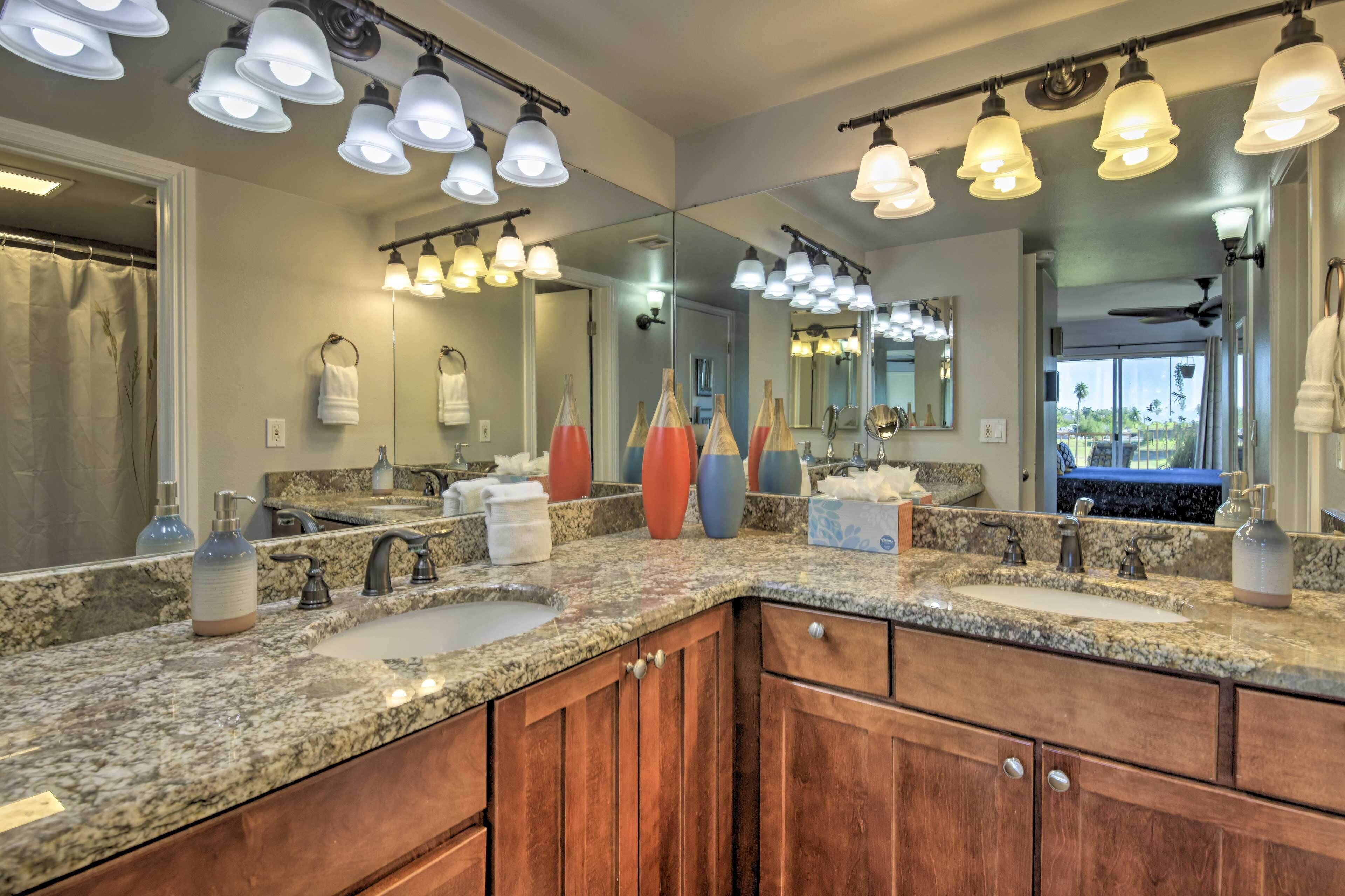 A bathroom with granite countertops, a double sink, wooden cabinets, and multiple light fixtures.