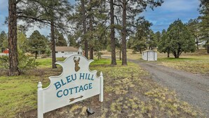 Schild für Bleu Hill Cottage mit einem Hirschkopf-Logo, umgeben von hohen Kiefern und einem Schotterweg.