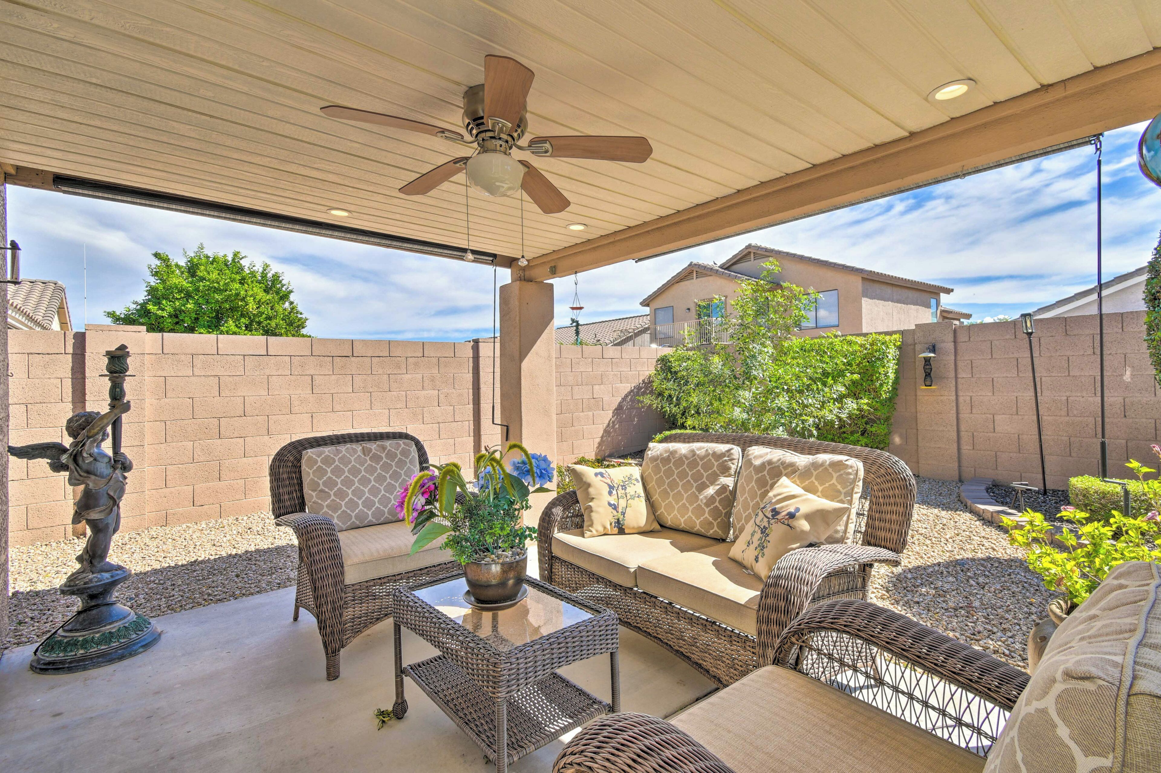 A covered patio area with wicker furniture, a ceiling fan, and a potted plant.