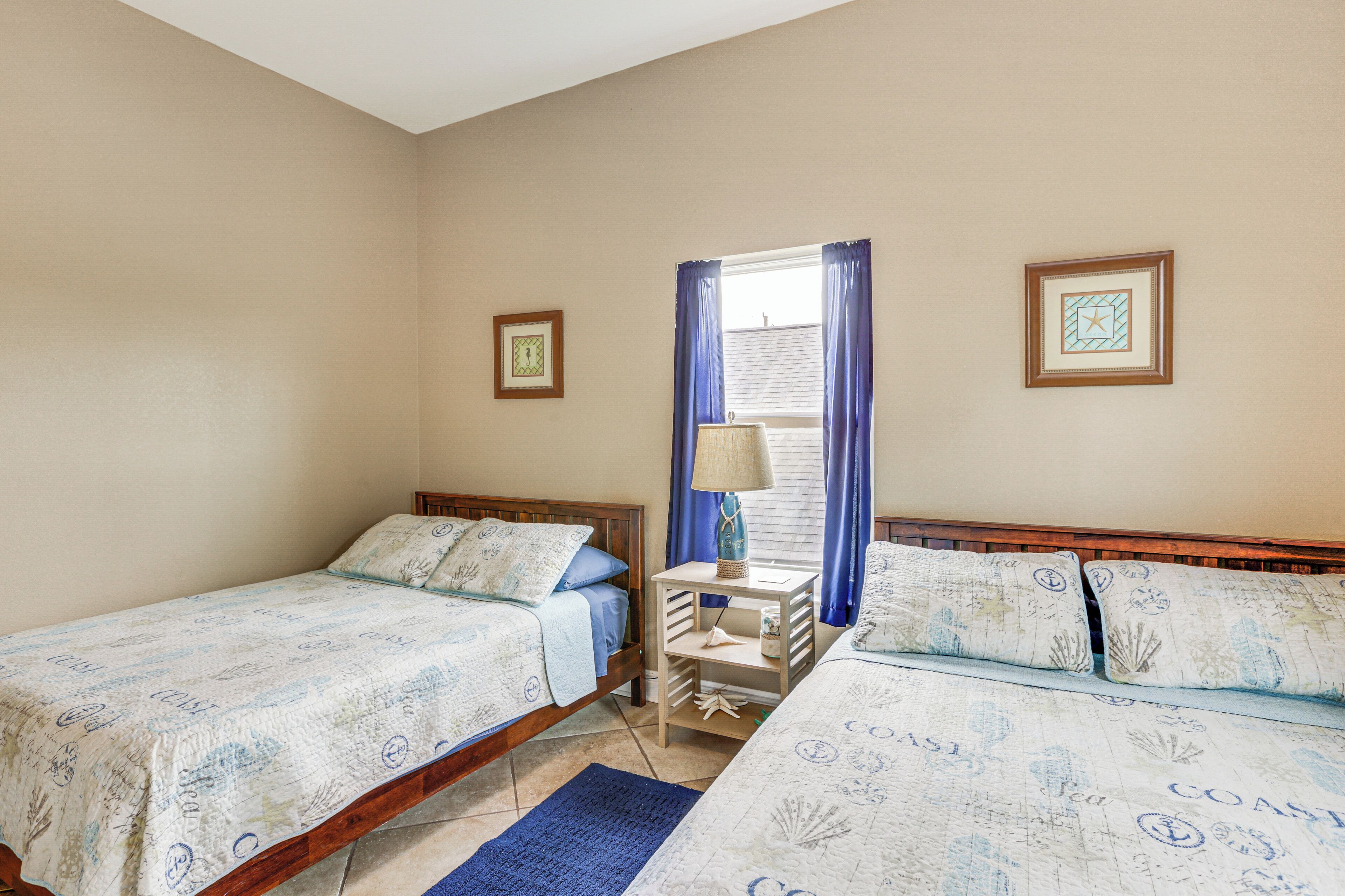 A bedroom with two single beds, a nightstand, a lamp, and a window with curtains.