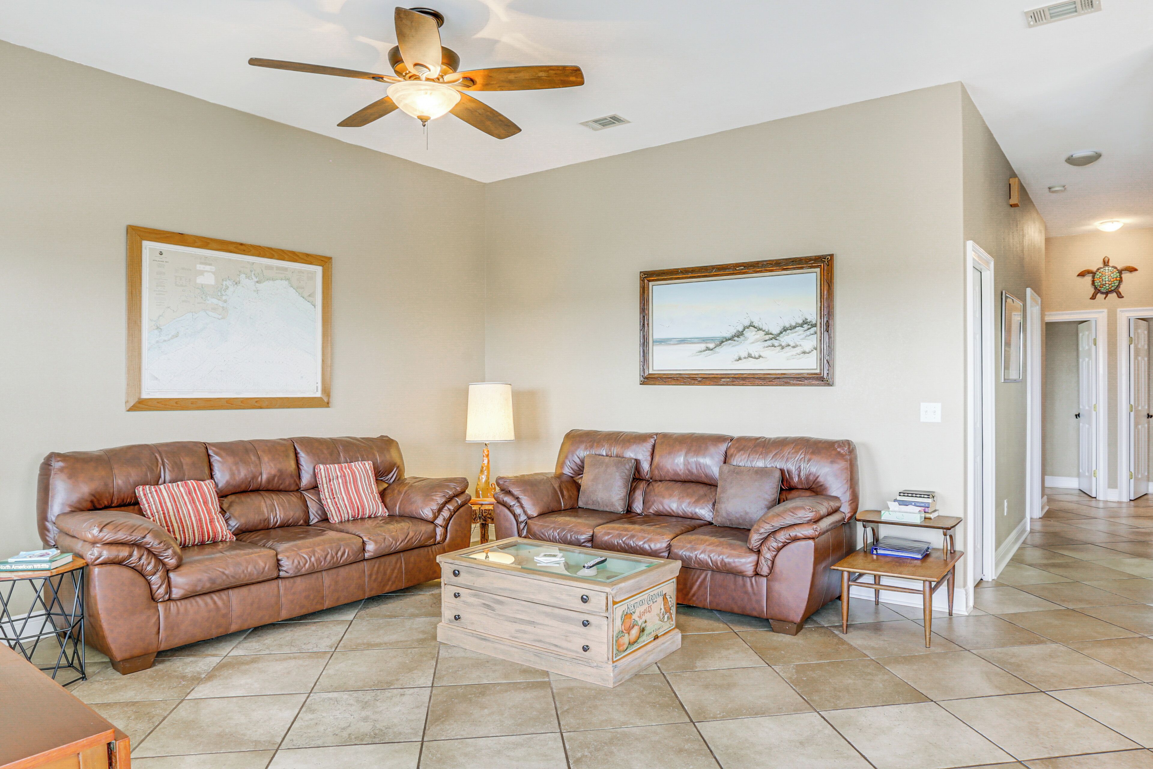 A spacious living room with two brown leather sofas, a wooden coffee table, and a ceiling fan.