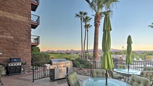An outdoor patio with a grill, chairs, and umbrellas, overlooking a scenic landscape.