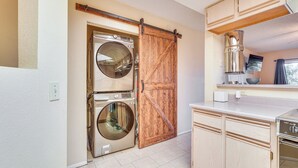 A laundry room with two front-loading washing machines, a wooden sliding door, and a countertop with a sink and a stove.