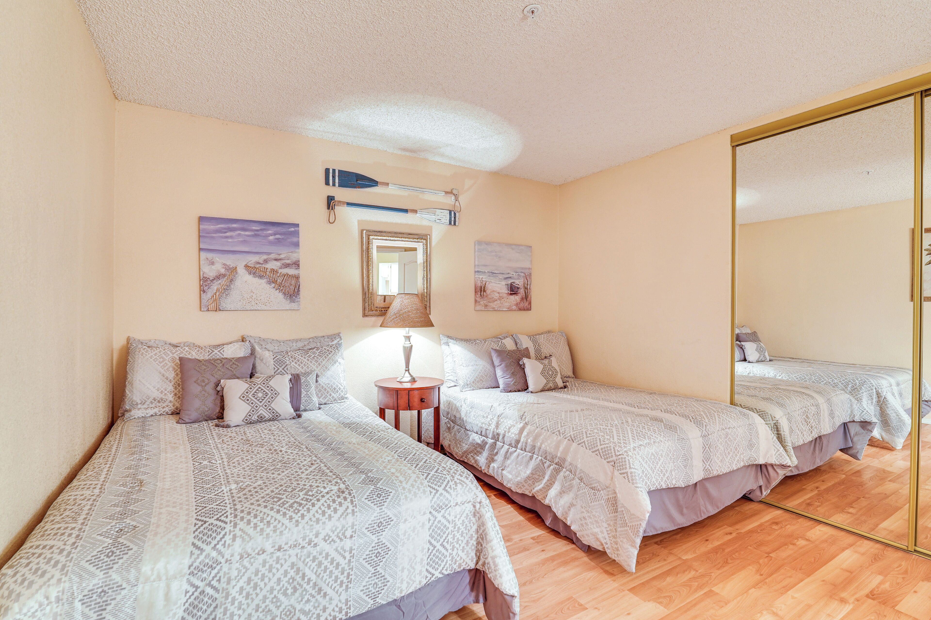 A bedroom with two beds, a mirror, and artwork on the walls.