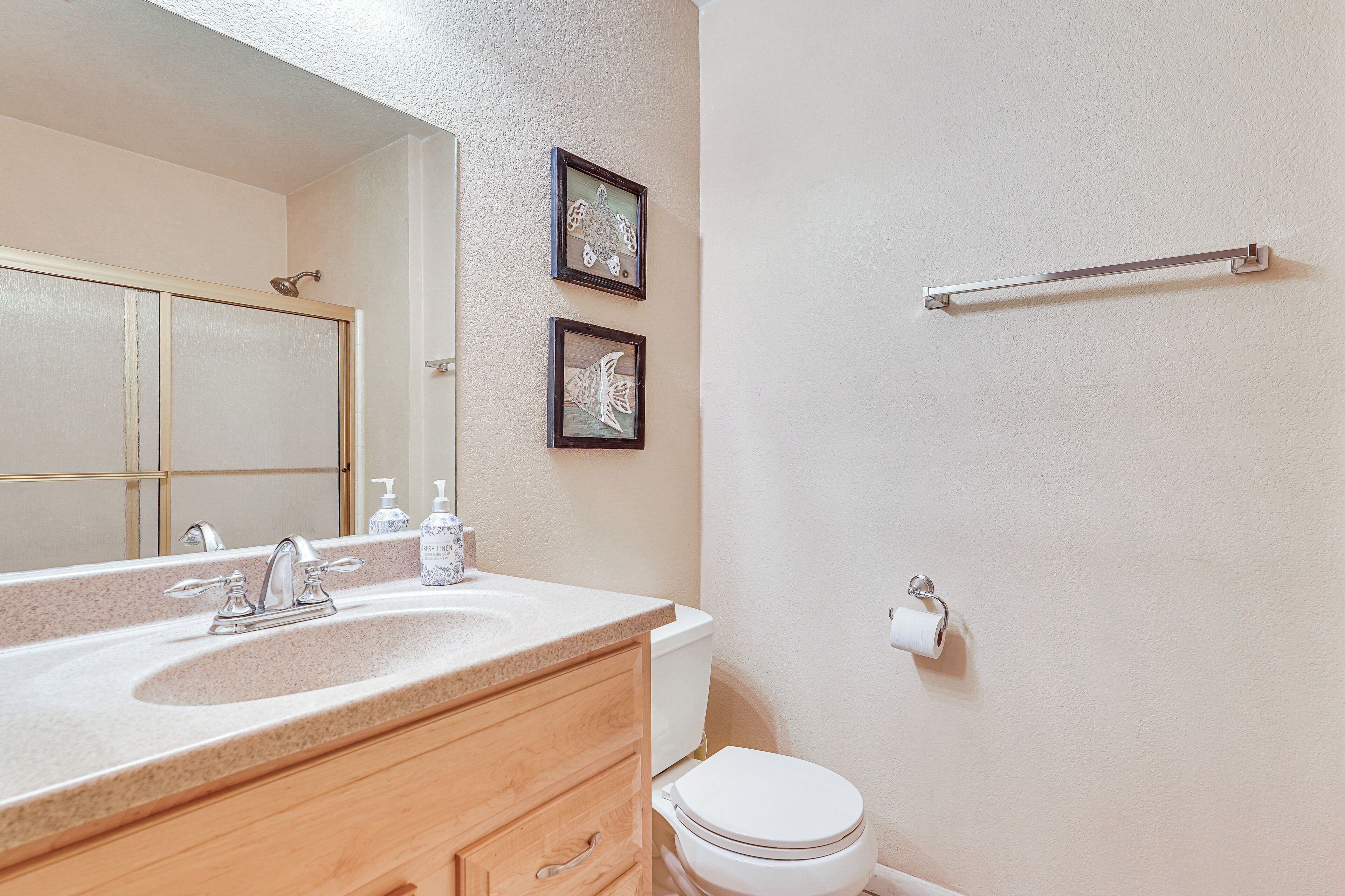 Une salle de bain avec un lavabo, un miroir, des toilettes et des tableaux encadrés accrochés au mur.