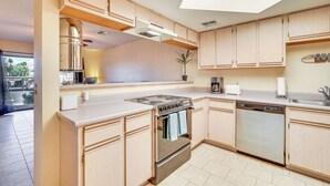A modern kitchen with light wood cabinets, stainless steel appliances, and a large window providing natural light.