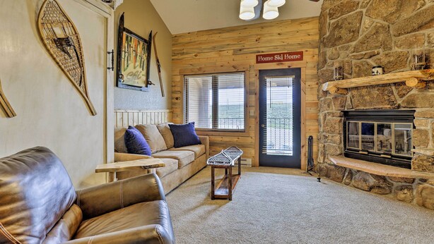 A cozy living room with a stone fireplace, a leather sofa, a wooden coffee table, and a sign reading "Home Ski Home". - Granby Condo w/ Pool Access, Near Hiking & Skiing! (Granby)