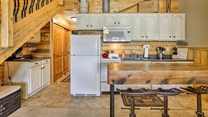 A rustic kitchen with wooden cabinets, a white refrigerator, a microwave, and a wooden dining table with stools. - Granby Condo w/ Pool Access, Near Hiking & Skiing! (Granby)