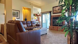 A living room with a brown leather sofa, a coffee table, a large potted plant, and a fireplace. - Oro Valley Getaway w/ Patio, BBQ & Mountain Views! (Oro Valley)