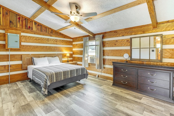 Un dormitorio tipo cabaña de troncos con cama, cómoda y ventilador de techo.