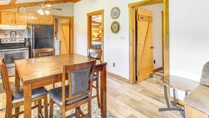 A wooden dining table with chairs, a refrigerator, and wooden cabinets in a kitchen area. - Rogersville Barn Apartment on 27 Acres w/ Pond! (Rogersville)