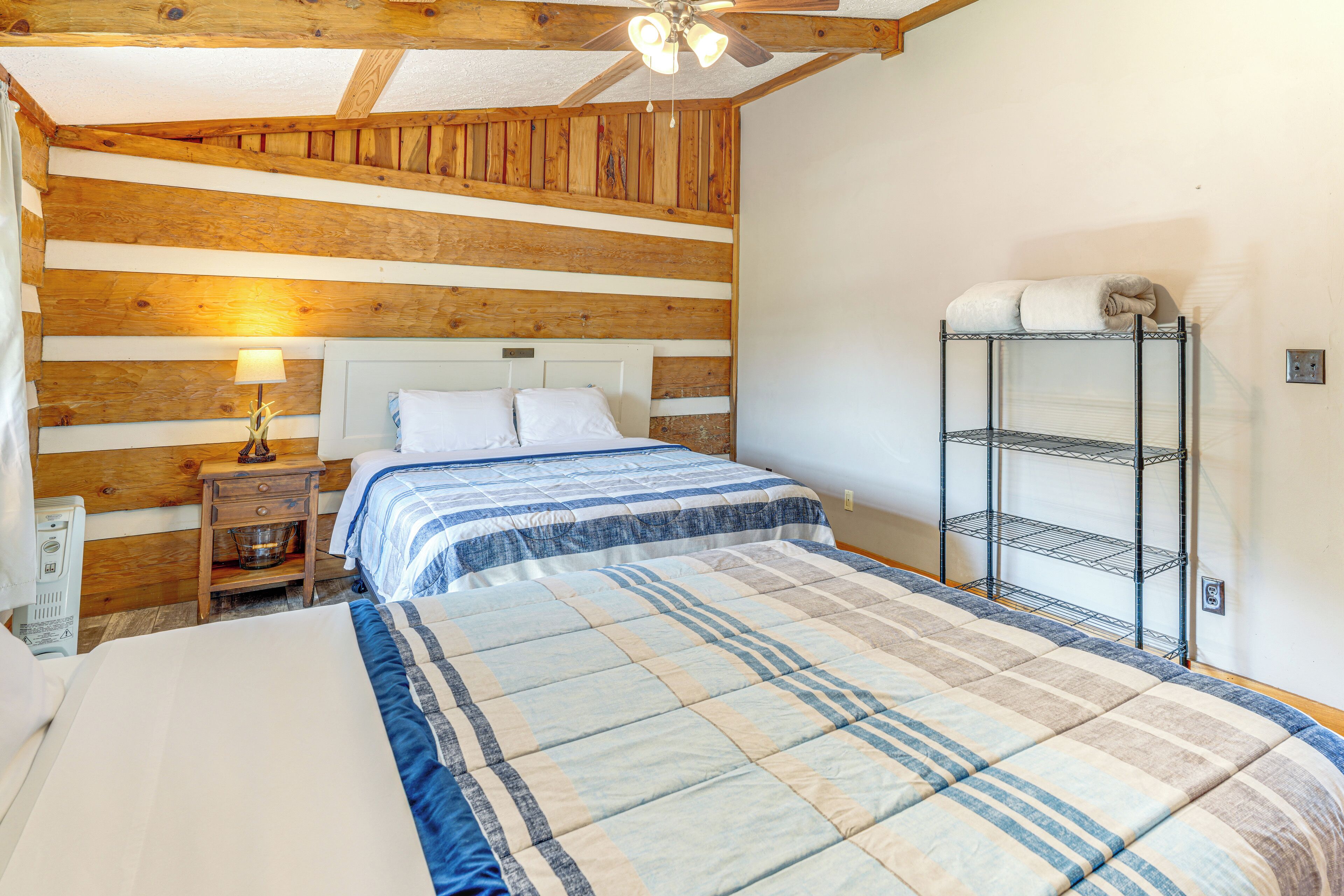 Una camera da letto con soffitto in legno, un letto con copripiumino a righe, un comodino con una lampada e un mobiletto a scaffali in metallo.