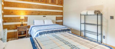 Una camera da letto con soffitto in legno, un letto con copripiumino a righe, un comodino con una lampada e un mobiletto a scaffali in metallo.