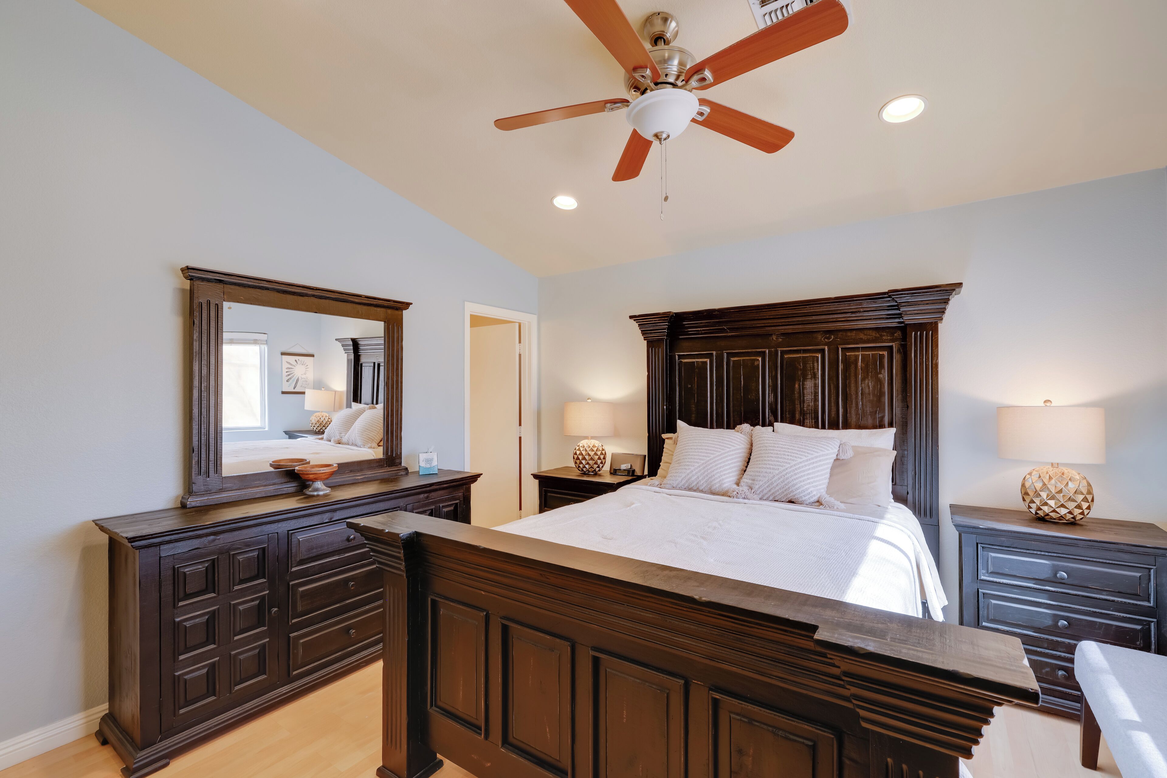 Un dormitorio con una cama grande, cabecera de madera oscura, ventilador de techo y mesita de noche con lámpara.