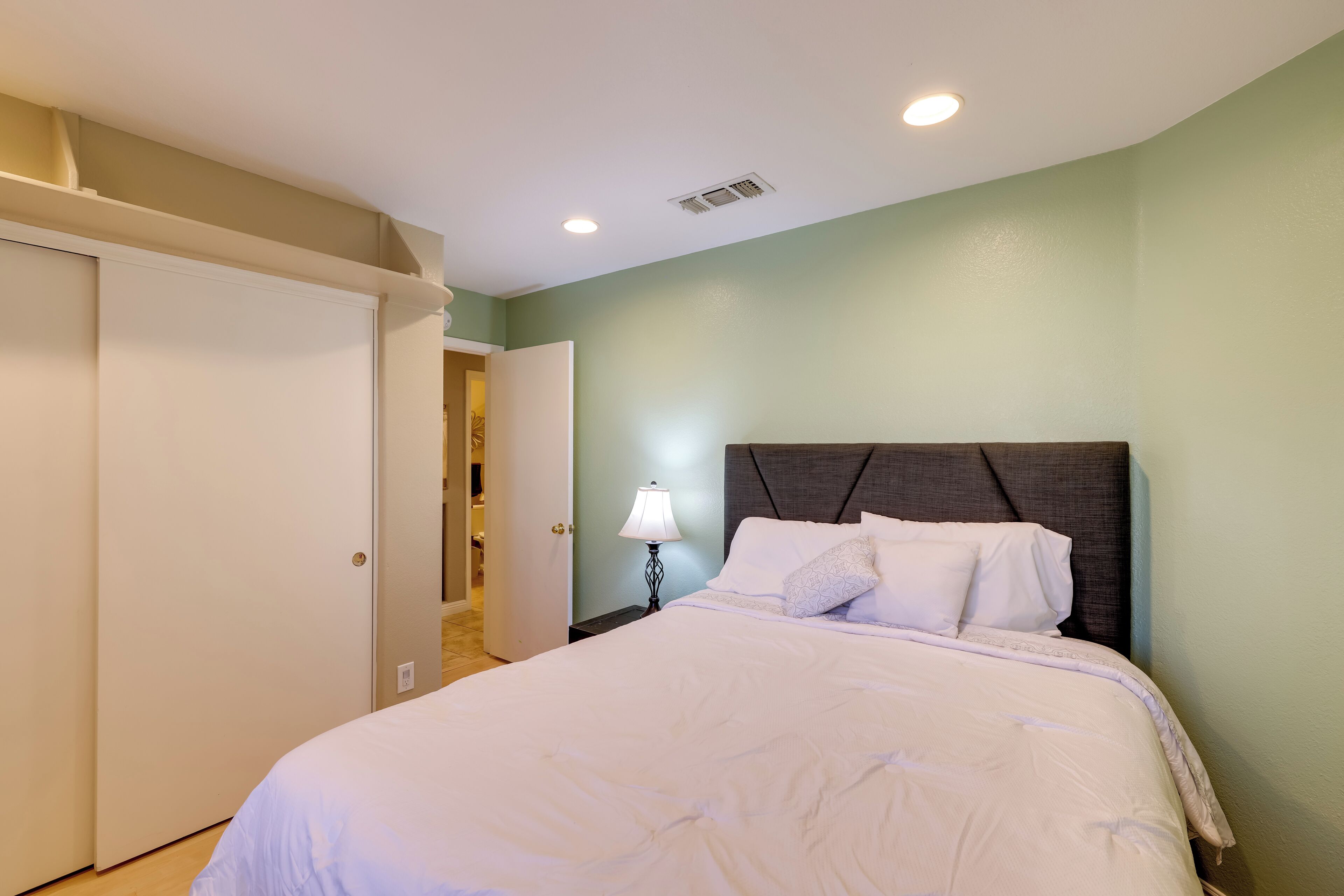 A bedroom with a bed, a nightstand, a lamp, and a door.