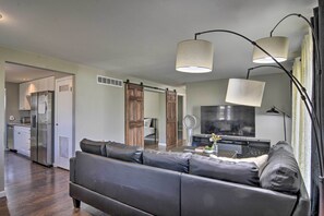 Un salon moderne avec un canapé en cuir foncé, un téléviseur à écran plat et un coin repas comprenant un réfrigérateur et des placards.