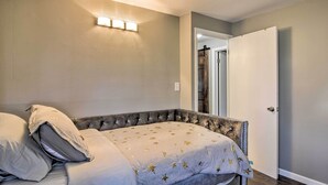 Une chambre à coucher avec une tête de lit capitonnée, un lit recouvert d’une couvre-lit à motifs et un luminaire fixé au mur.