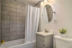 A bathroom with a bathtub, a white sink, a toilet, a mirror, and a potted plant. - Buffalo Getaway w/ Charcoal Grill & Patio! (Buffalo)
