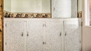 A set of white cabinets with a speckled pattern, a small refrigerator on top, and a decorative tile border with bear illustrations.