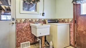 A small, compact bathroom with a vintage design, featuring a sink, a washing machine, and a decorative wall with a floral pattern.