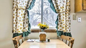 A wooden dining table with two chairs, a vase with yellow flowers, and a window with curtains.