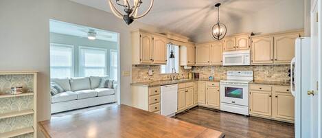 A spacious kitchen with wooden flooring, light-colored cabinetry, a central island, and pendant lighting.