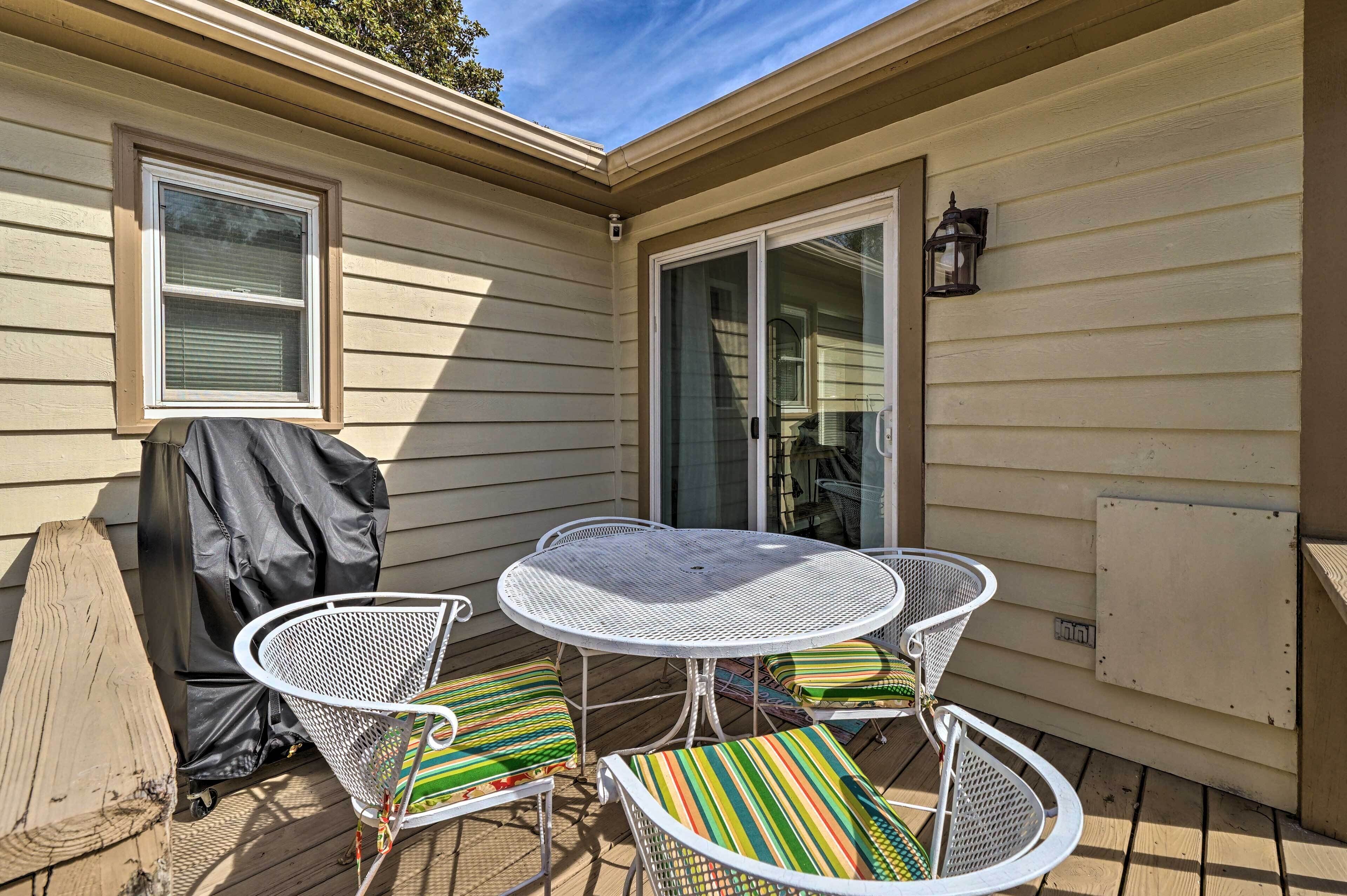 A patio with a round metal table and chairs, a barbecue grill, and a sliding glass door.