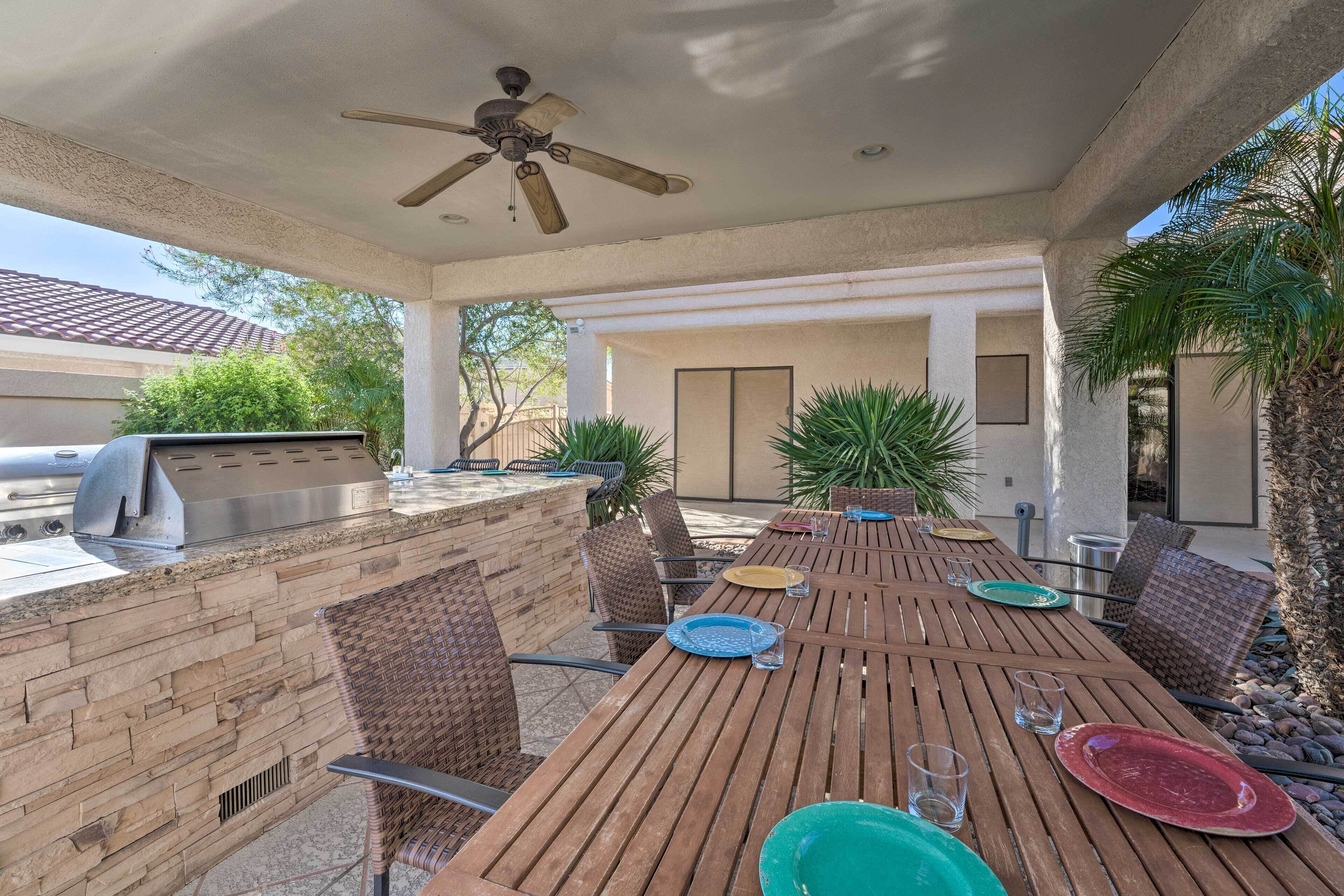 An outdoor patio with a wooden table, chairs, a grill, and a ceiling fan.